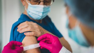 A doctor places a bandaids on a patient's arm after giving them a shot