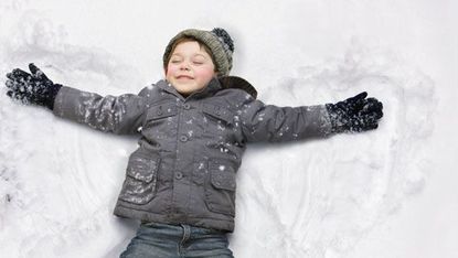 A young boy making snow angels.