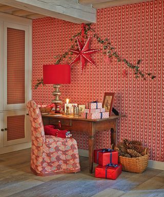 Christmas wall decor ideas with a red star and foliage garland strung over a present-laden desk, with red wallpaper