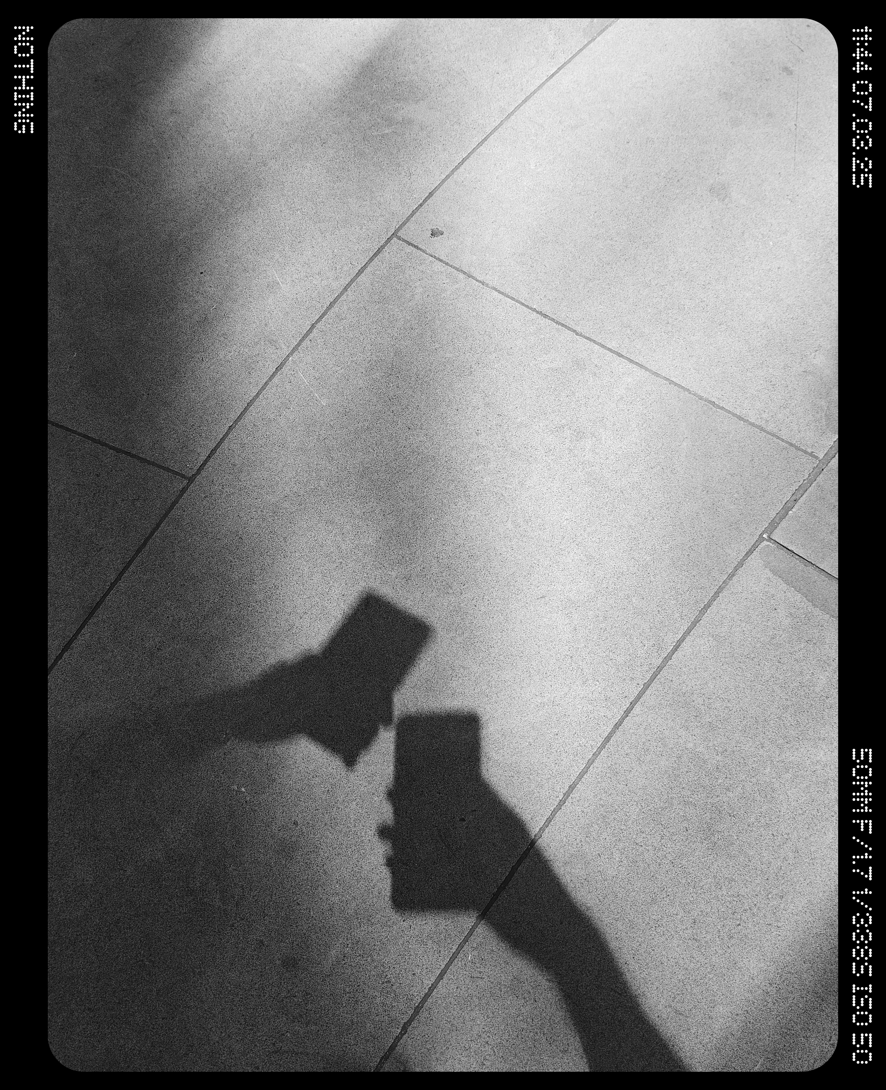 Two hands holding phones casting a shadow over paving slabs