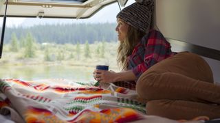 A woman camping in her car drinks coffee and enjoys the view