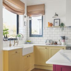 White painted and tiled kitchen with yellow bottom cabinets and a white worktop