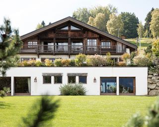 A green roof on the terrace of a dark wood chalet-style property with large lawn.