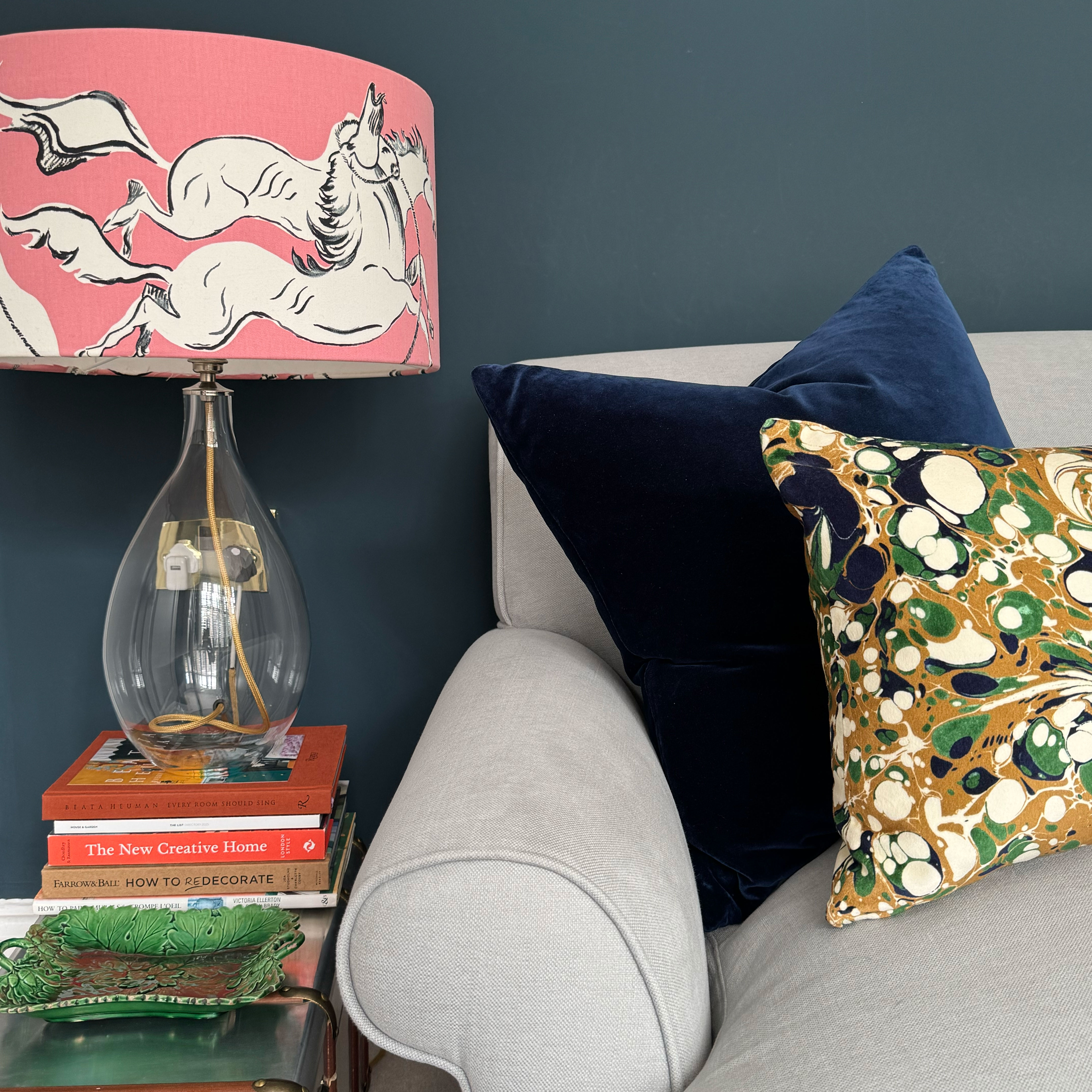 Close up of glass table lamp with pink patterned shade on pile of books on side table