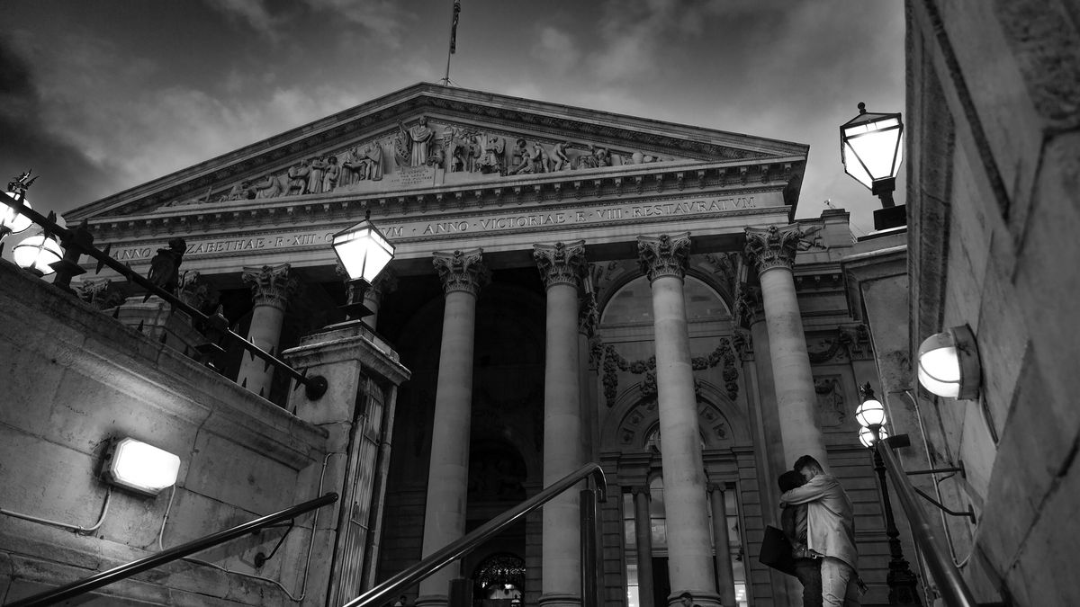 Black and white image of a person ascending steps to a grand building with columns and ornate facade