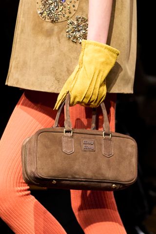 a detail image of a Miu Miu model carrying a brown suede Arcadie bag on the runway