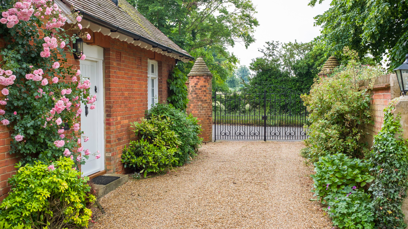 gravel driveway with iron gates at the end of flowers on building to the left