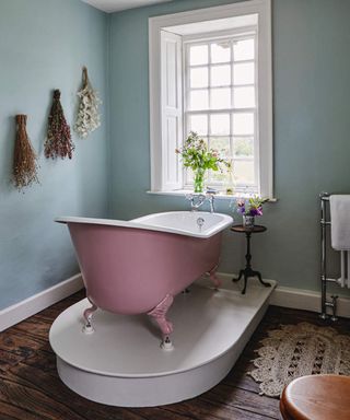 A pink slipper bathtub in bathroom with blue-green wall paint decor and dried flowers