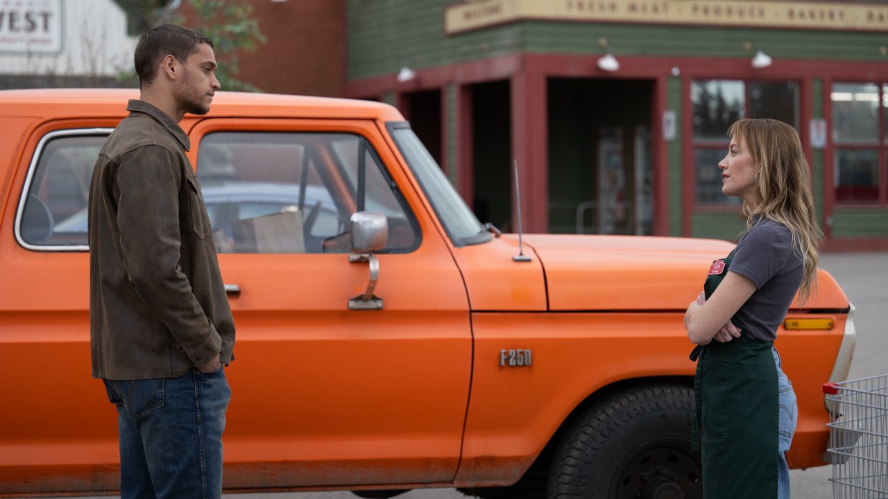 オレンジ色のトラックの前に立って見つめ合うレジャーとケンナ。