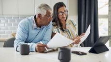 An older couple is sitting at their kitchen table reviewing financial documents.