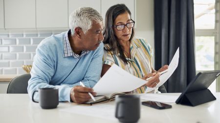 An older couple is sitting at their kitchen table reviewing financial documents.