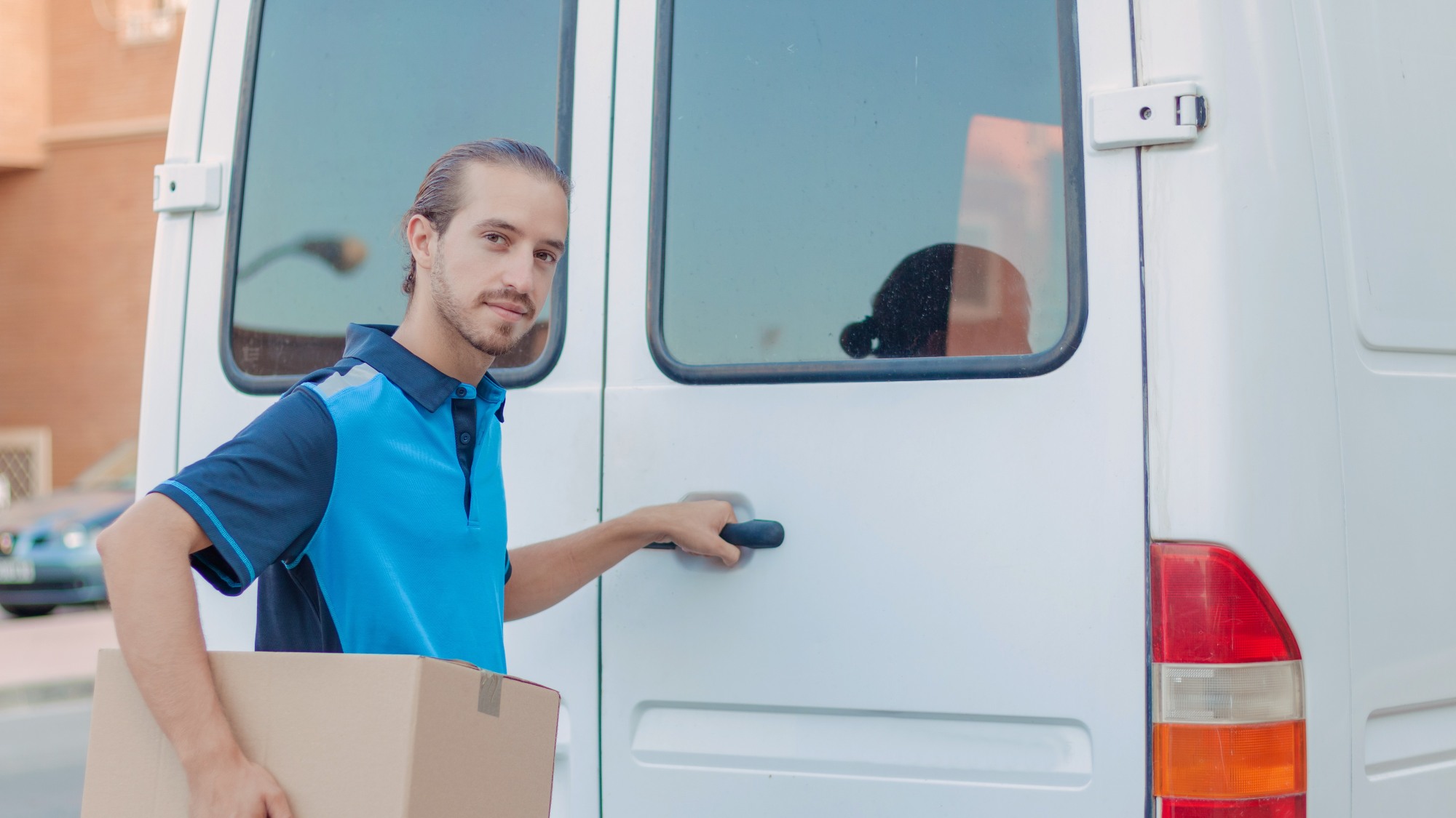 Delivery man holding a box and opening a van, smiling and relaxed