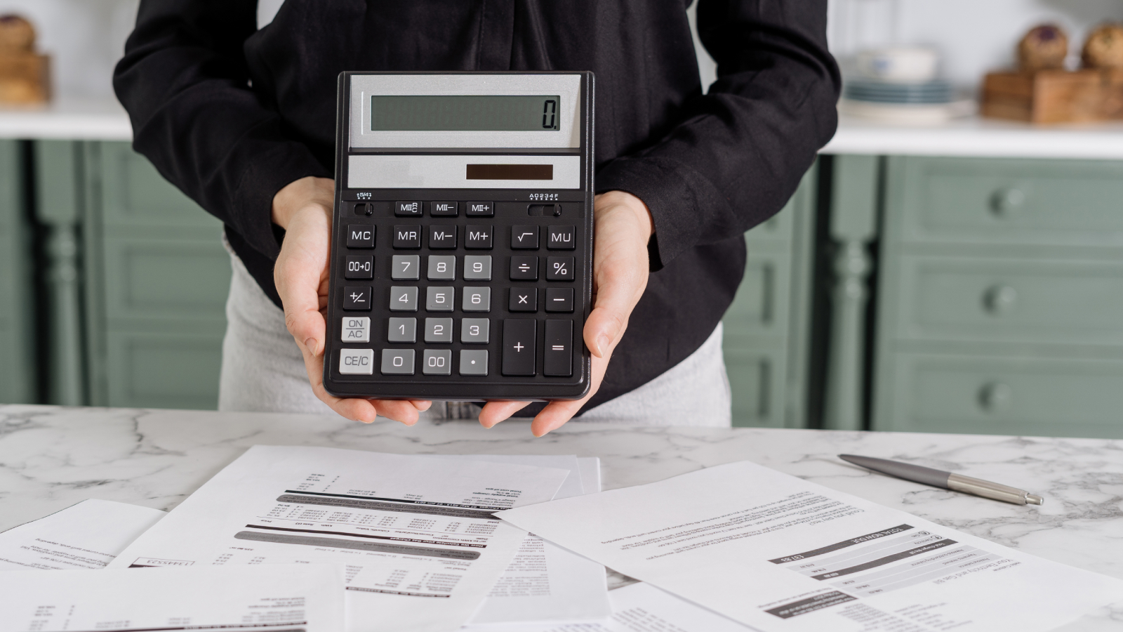hands holding calculator displaying zero above paper bills on table 