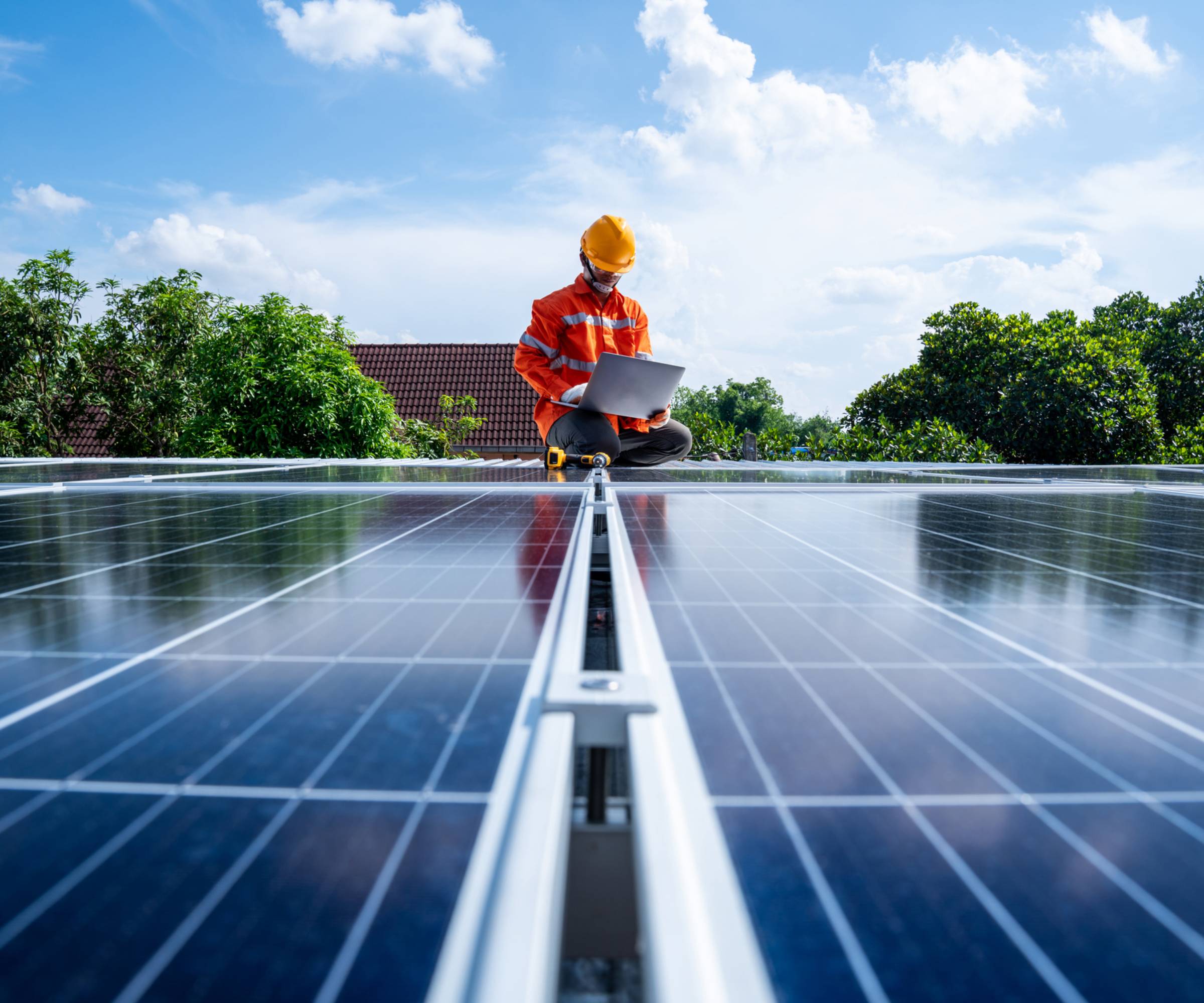 solar panel installer stood with laptop in front of solar panels