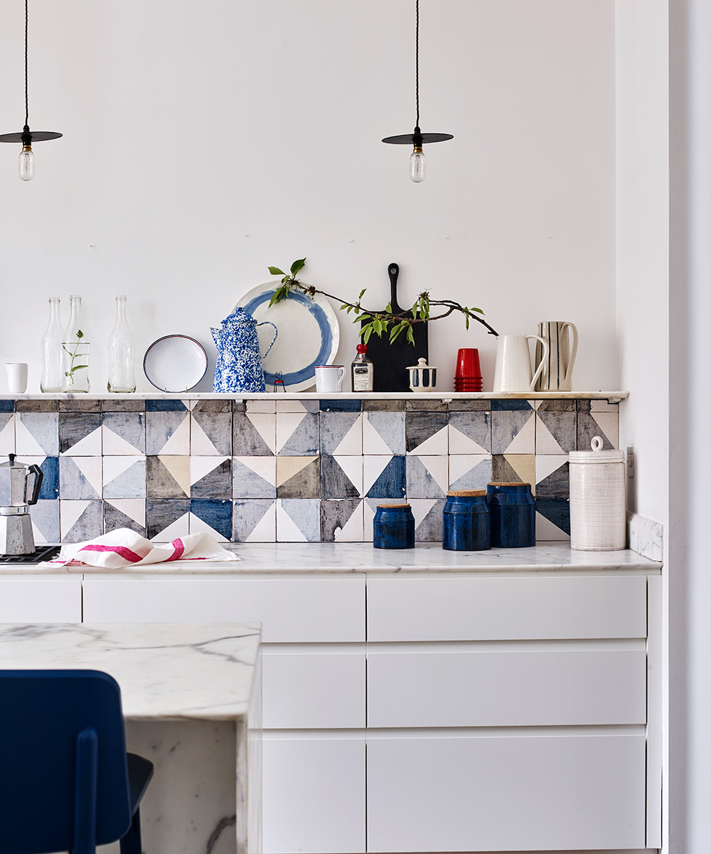 A close up of a marble worktop with sleek white cabinets and abstract mosaic tiles