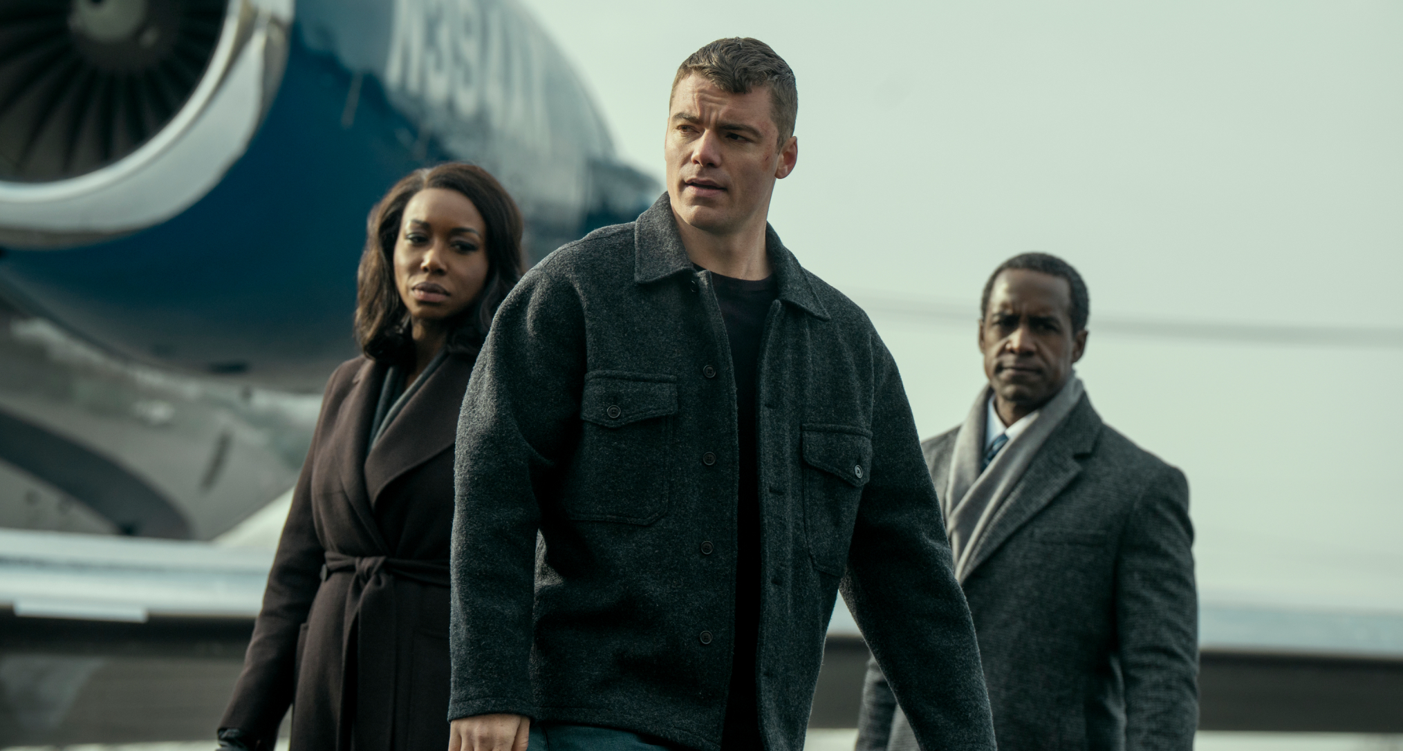 amanda Warren as Catherine Weaver, Gabriel Basso as Peter Sutherland, Albert Jones as Deputy Director Aiden Mosley standing outside of a plane on a jetway in the night agent season 3