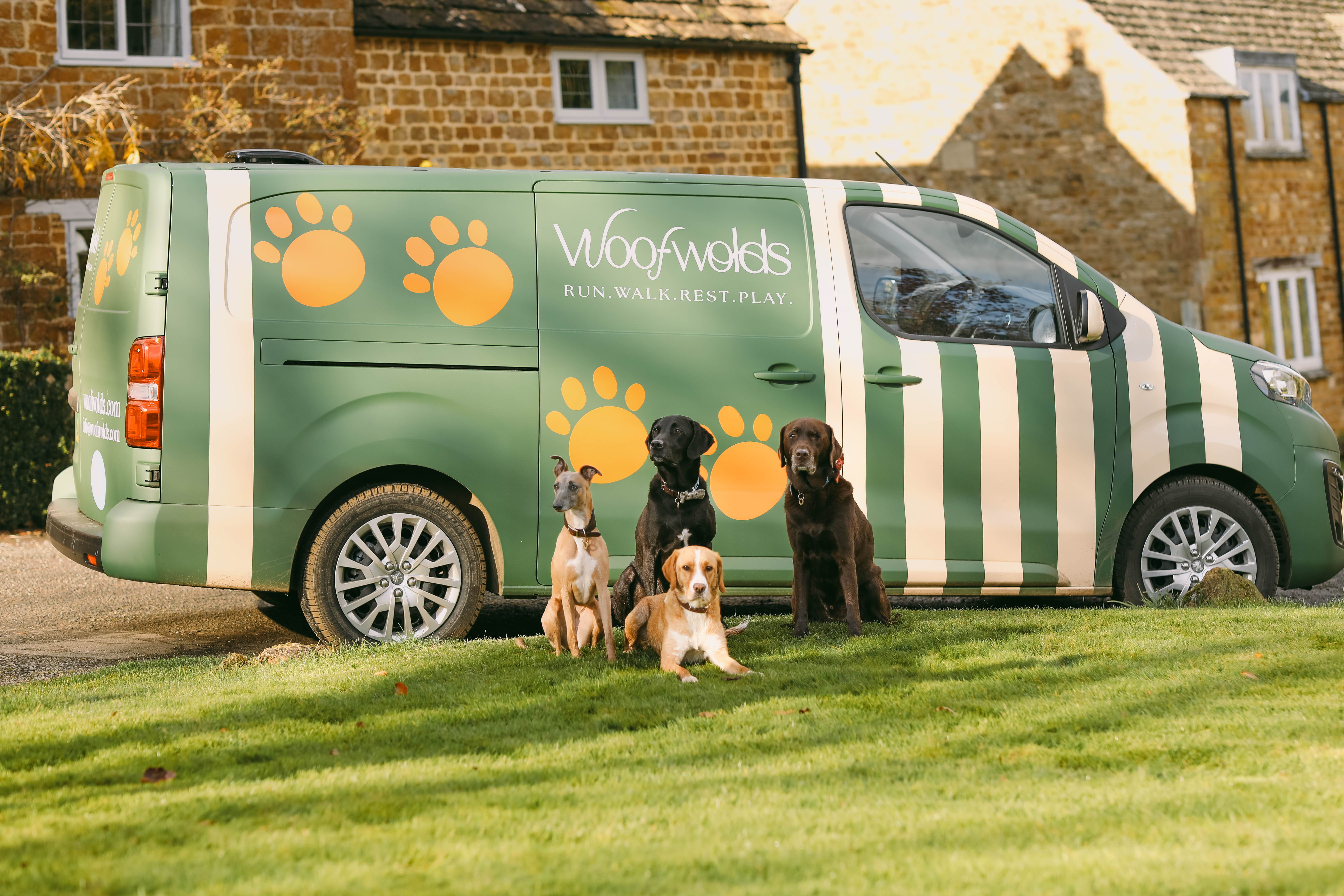 Four dogs sit in front of a woofwolds branded van, which is green and white stripey