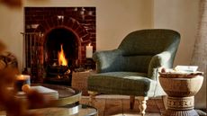 An upholstered green armchair beside a brick fireplace in a cream living room. 