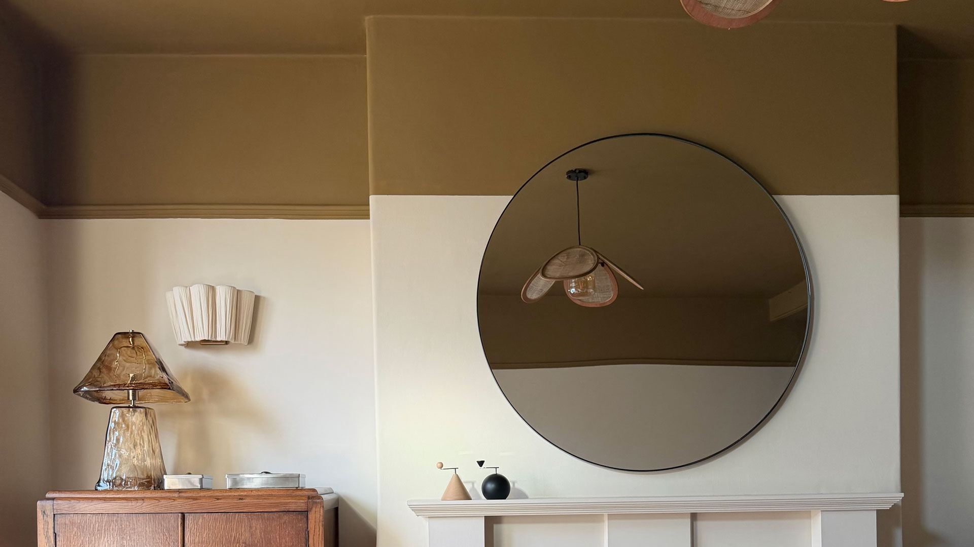 Close up of a dining room with off-white walls, olive green ceiling and a large circular wall mirror