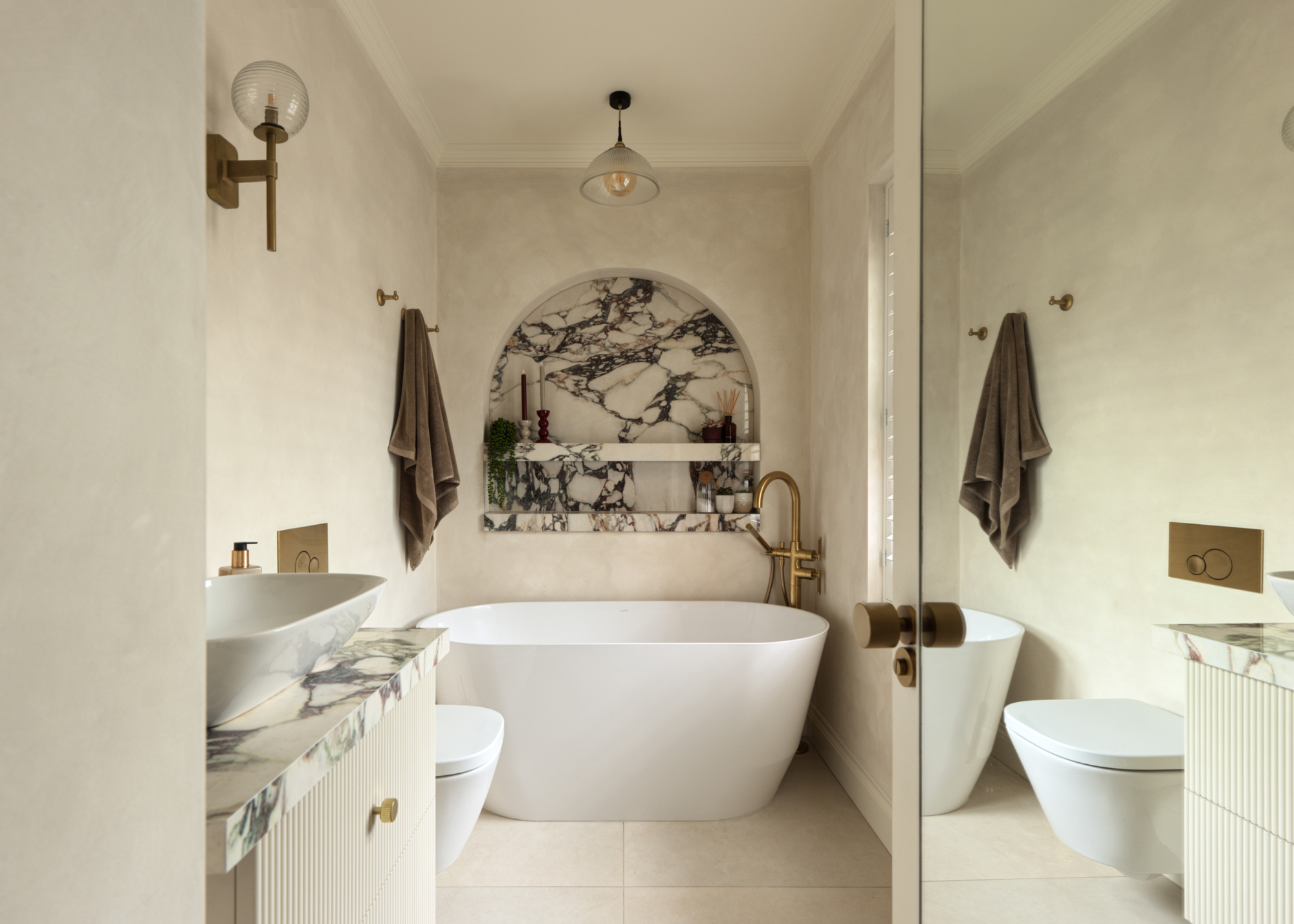 A spa like neutral bathroom with an atched niche centred over the bath tub in striking marble