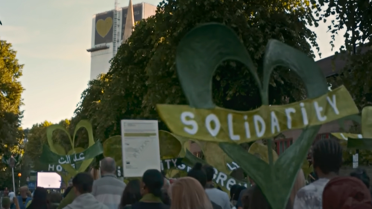 Protestors holding a sign that says &quot;solidarity&quot; in Grenfell: Uncovered