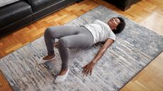 Woman performing bridge exercise on rug in domestic setting