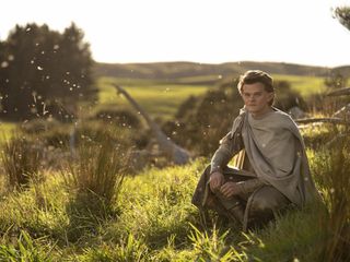 Robert Aramayo (Elrond) sits in a sunny field in The Lord of the Rings: The Rings of Power