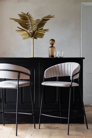 Two velvet bar stools with fluted backrests sit in front of a bar area
