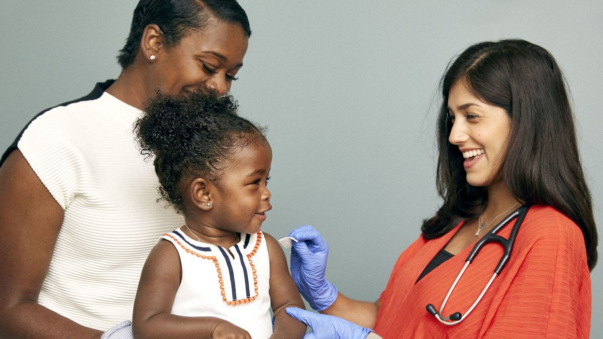 A smiling doctor prepares to deliver a vaccine to a happy toddler.