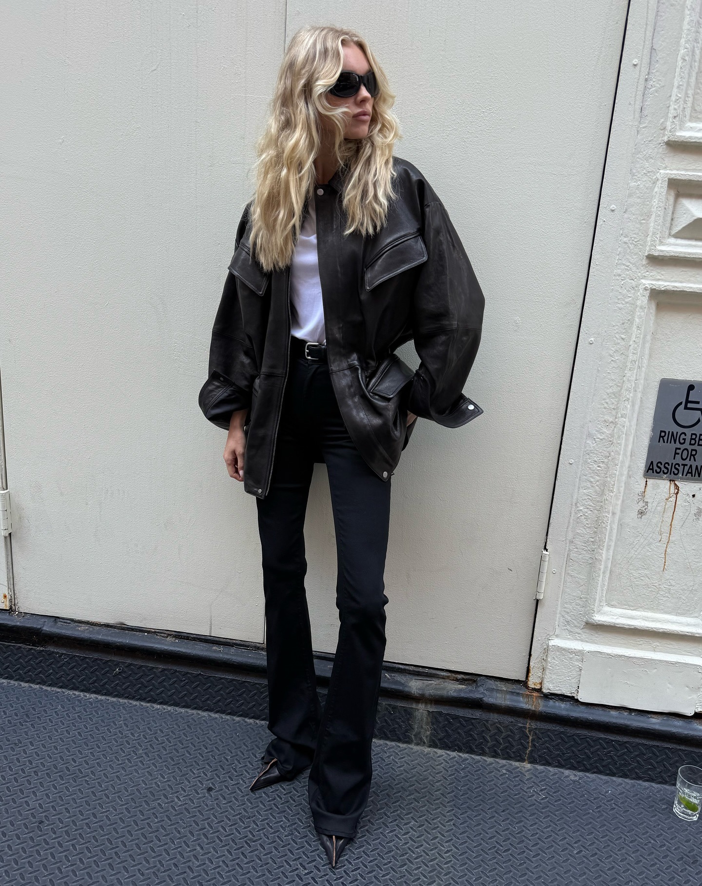 Elsa Hosk wearing a leather jacket, white top, and black bootcut jeans with Prada heels.