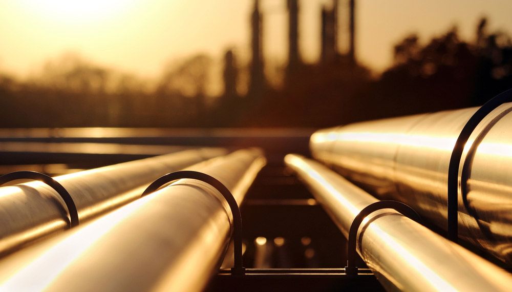 Pipelines in the foreground with an oil refinery in the background.