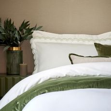 Close up of corner of made up bed with scallop trimmed pillows