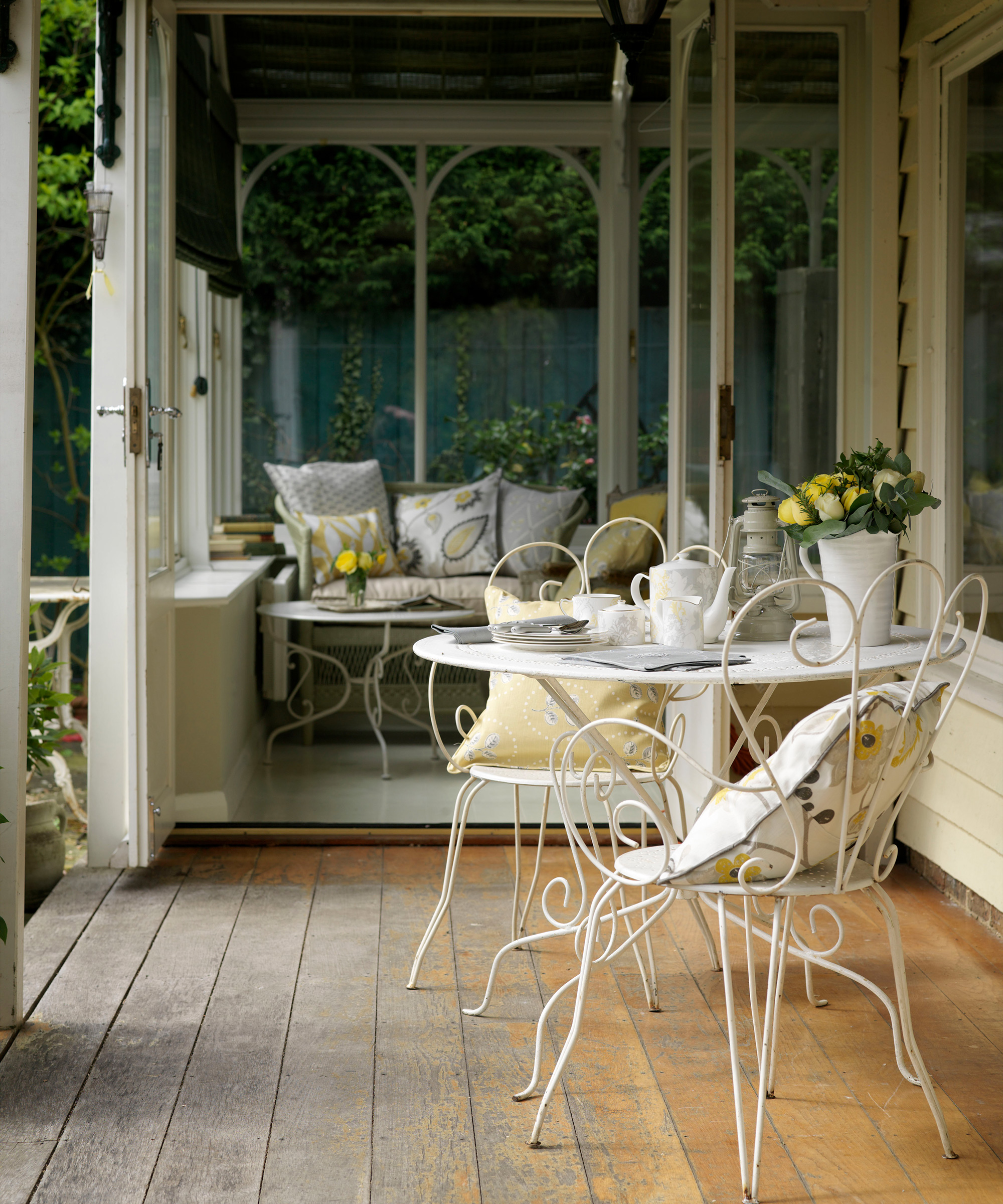 A porch area with wooden flooring, a metal bistro table and chair set and a sofa in the background