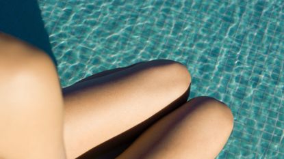woman's shoulder and legs seen over pool water, high angle view