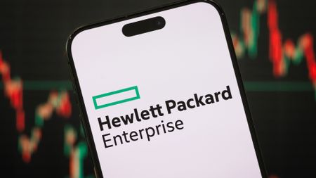 Hewlett Packard Enterprise (HPE) logo pictured on a smartphone with stock market graph fluctuations in background.