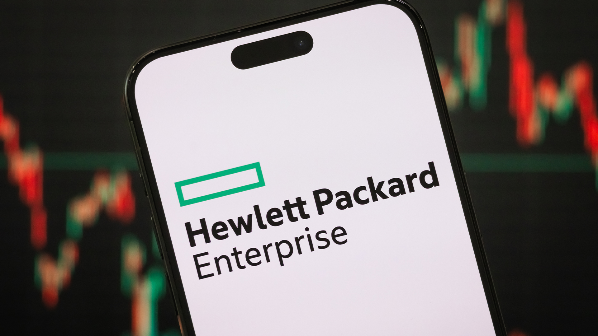 Hewlett Packard Enterprise (HPE) logo pictured on a smartphone with stock market graph fluctuations in background.