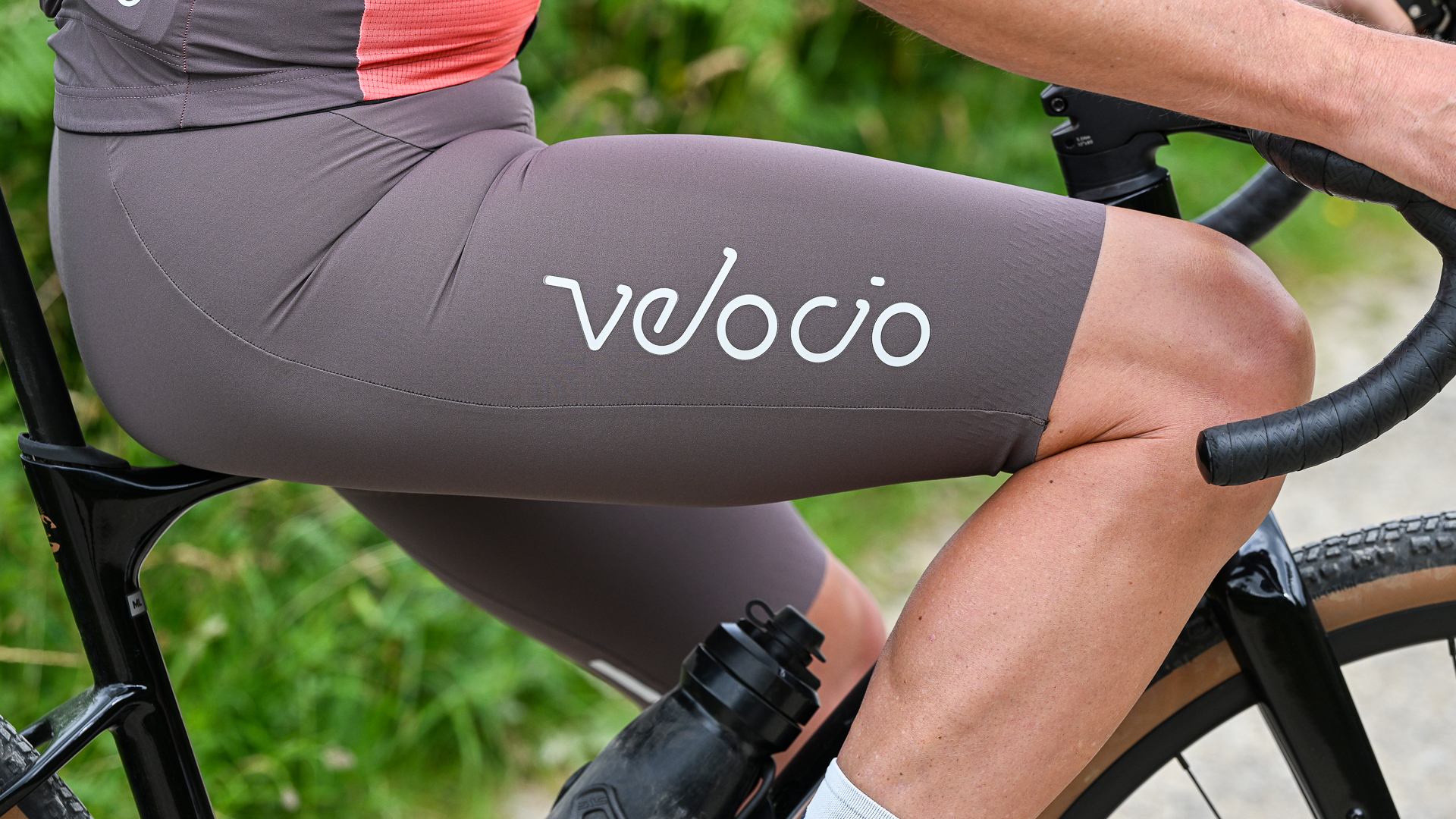 close up of a pair of brown shorts with the word 'Velocio' down the side on a man sitting on a bike's top tube