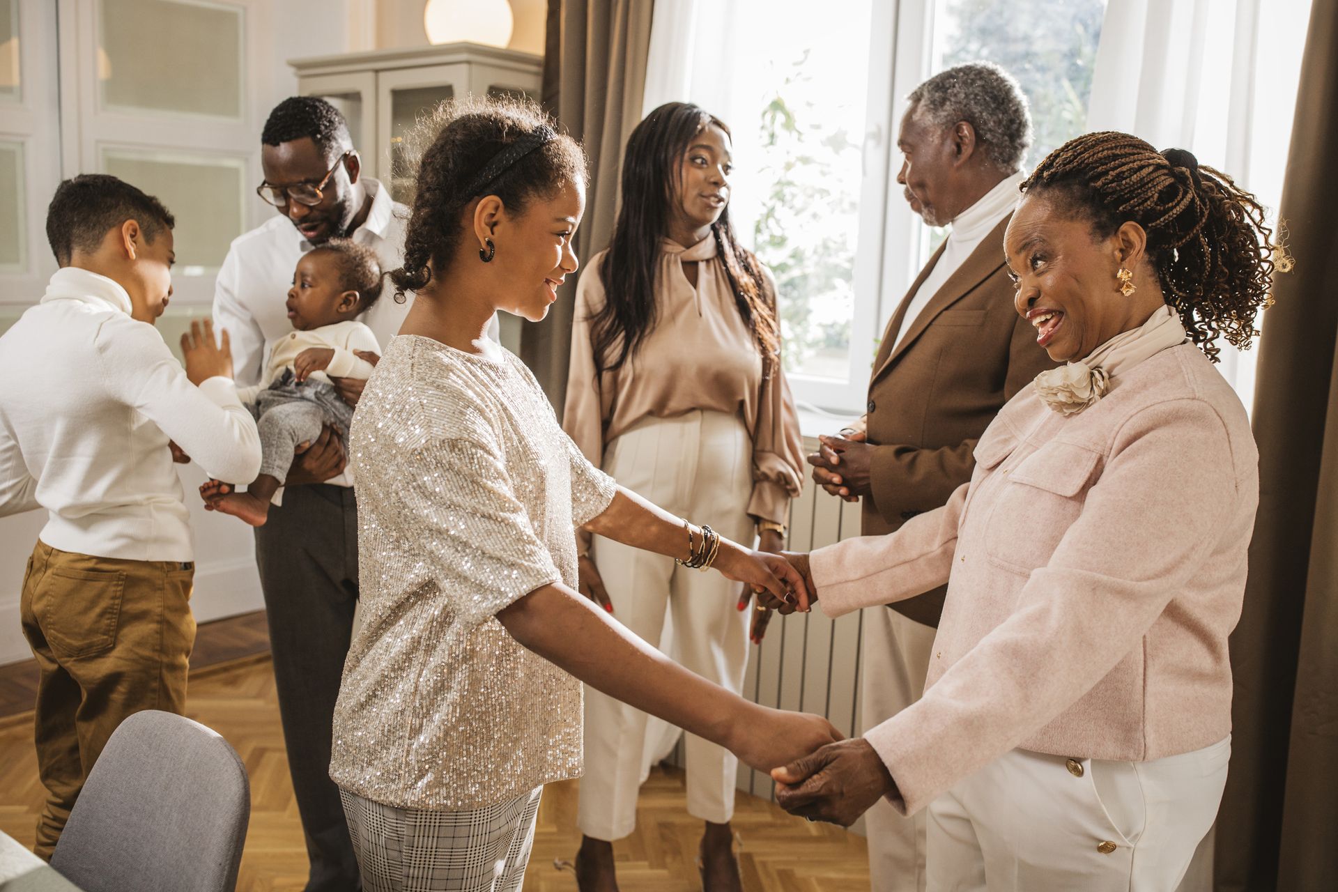 A multigenerational family greets each other standing up and dressed nicely for a meal.