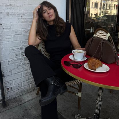 Kathryn Zahorak sitting at a red table wearing black top, black pants, and black boots 