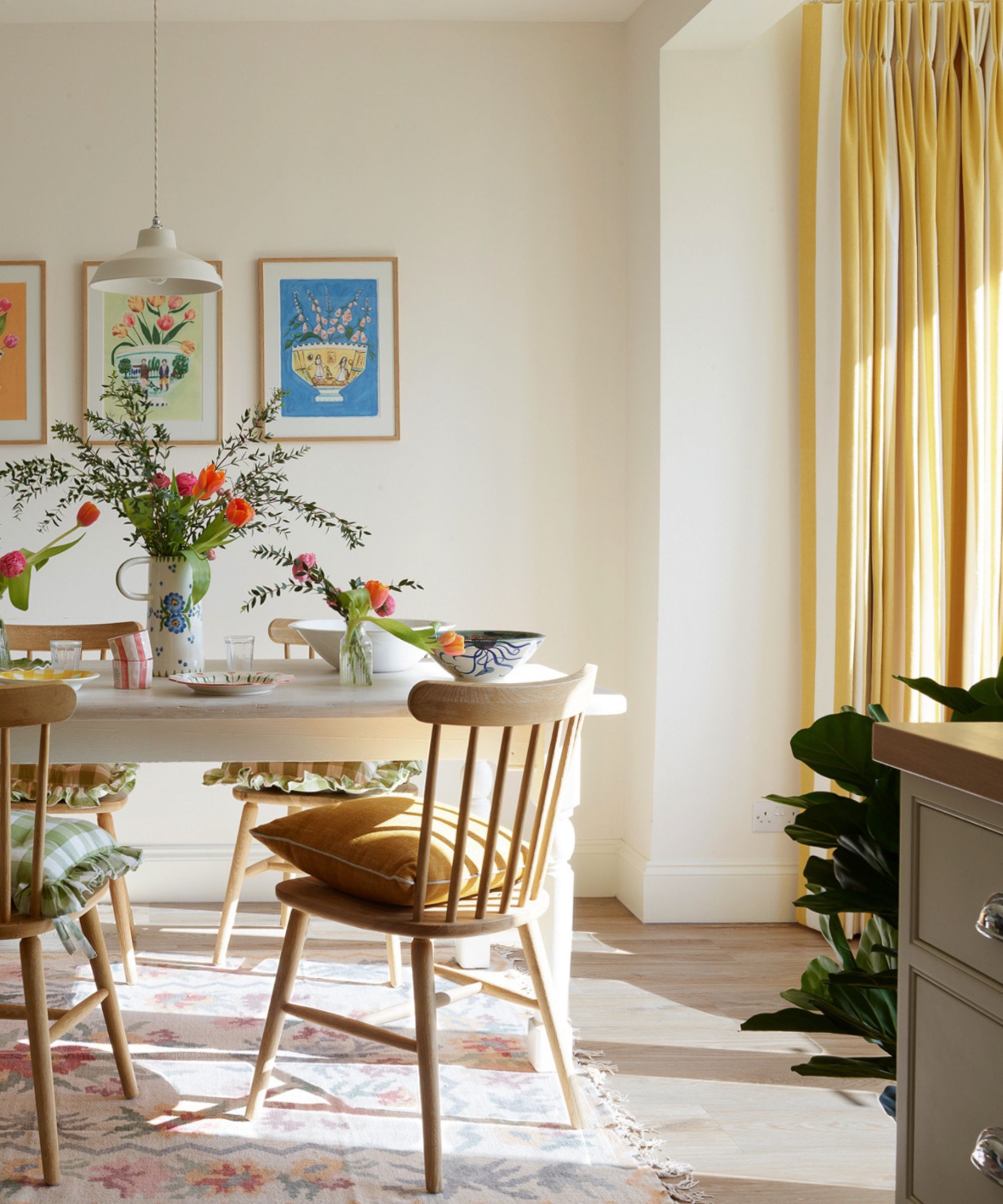 Scandi style dining room with white walls, white wooden table, wooden dining chairs, yellow curtains, and floral rug