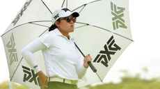 Auston Kim holding a PXG umbrella and wearing a white cap, sunglasses and white shirt
