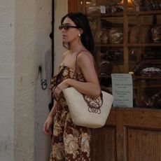 Woman wears floral trop and trousers, carries basket bag