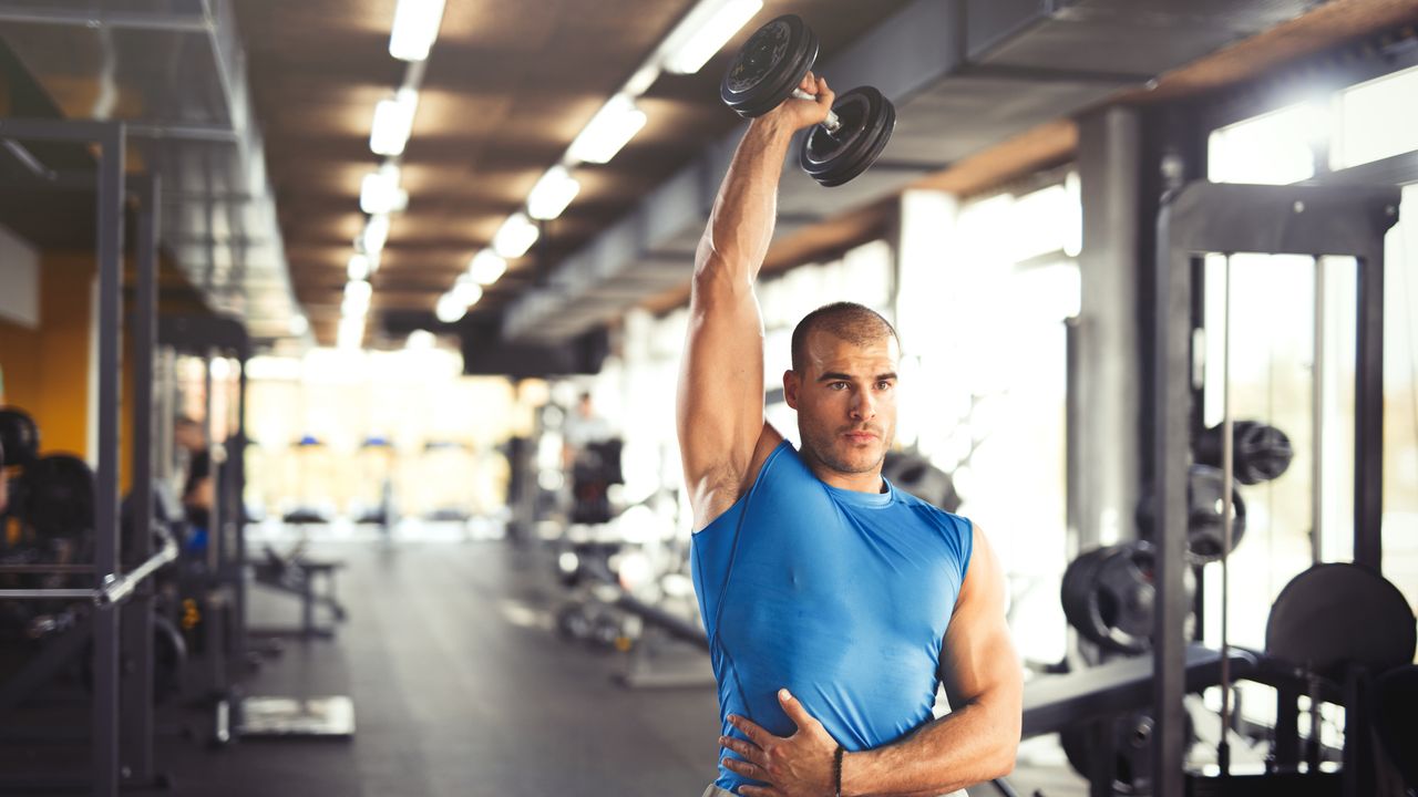 Young muscular man lifting up dumbbells at the gym