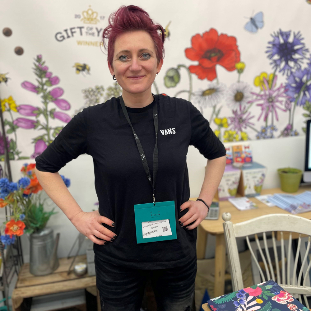 woman with short red hair stood against painted backdrop of flowers