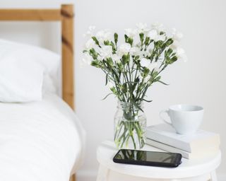 white nightstand with white flowers and a phone next to bed