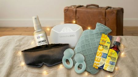 A group of sleep essentials from Amazon, displayed on a bed, with Christmas lights and a travel suitcase in the background.