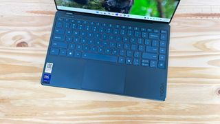 The keyboard deck of the Lenovo Yoga Slim 9i seen from above on a wood table