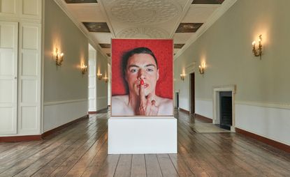 Inside an exhibition hallway with a large image featuring a male face and an index finger pushing against his lips. 