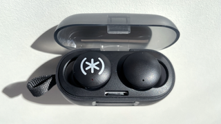 The Speck Gemtones Play earbuds sitting inside their charging case with the lid open, on a white tabletop.