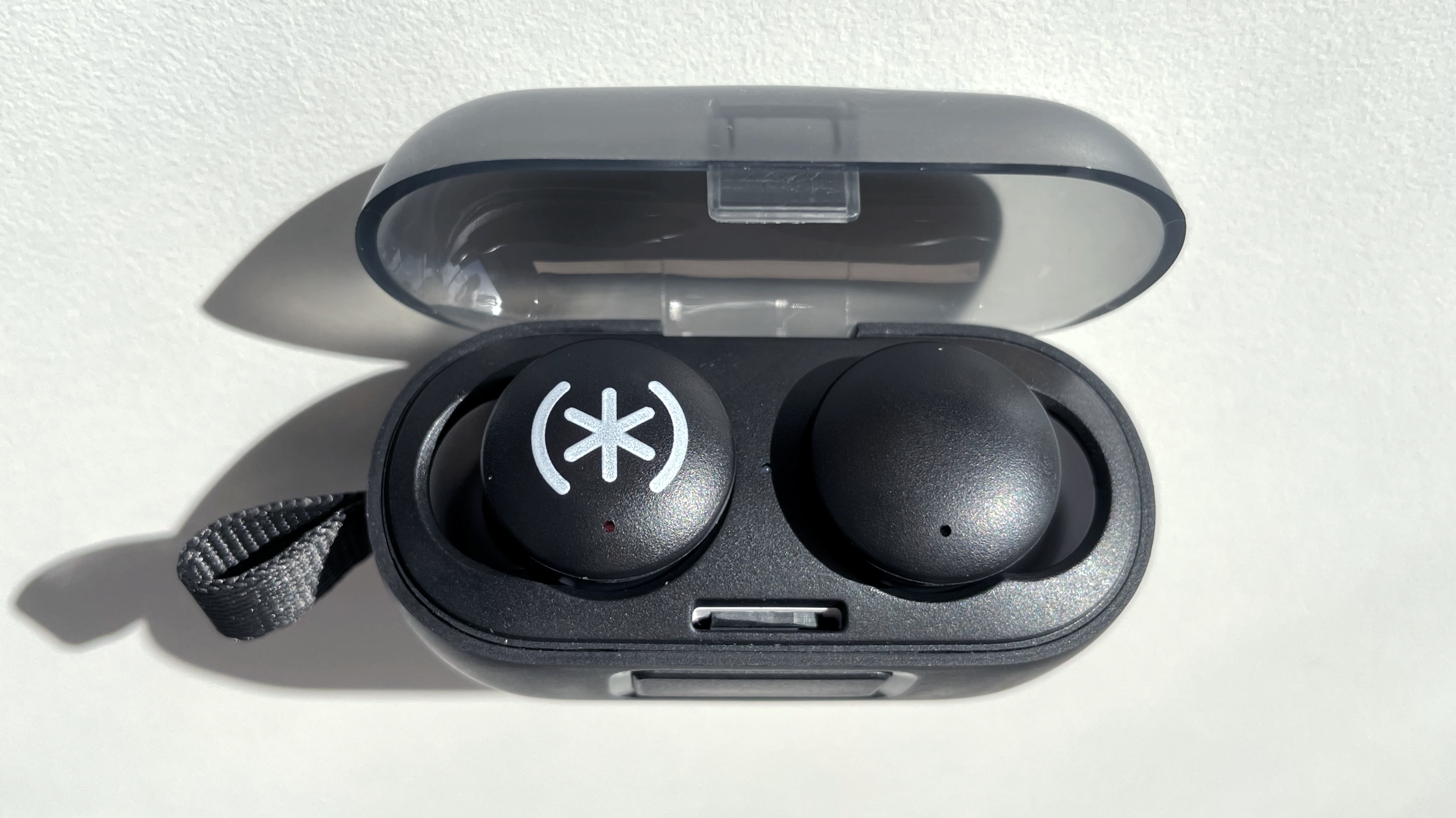 The Speck Gemtones Play earbuds sitting inside their charging case with the lid open, on a white tabletop.